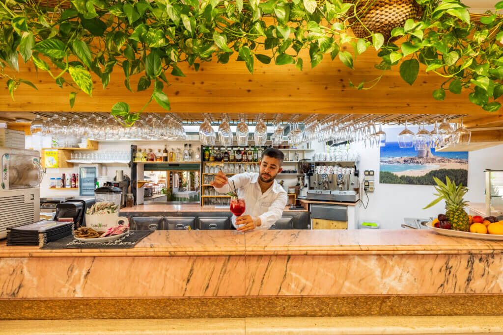 Galleria - Il bancone del bar dell'Hotel Domus de Janas con un barista che prepara uno spritz