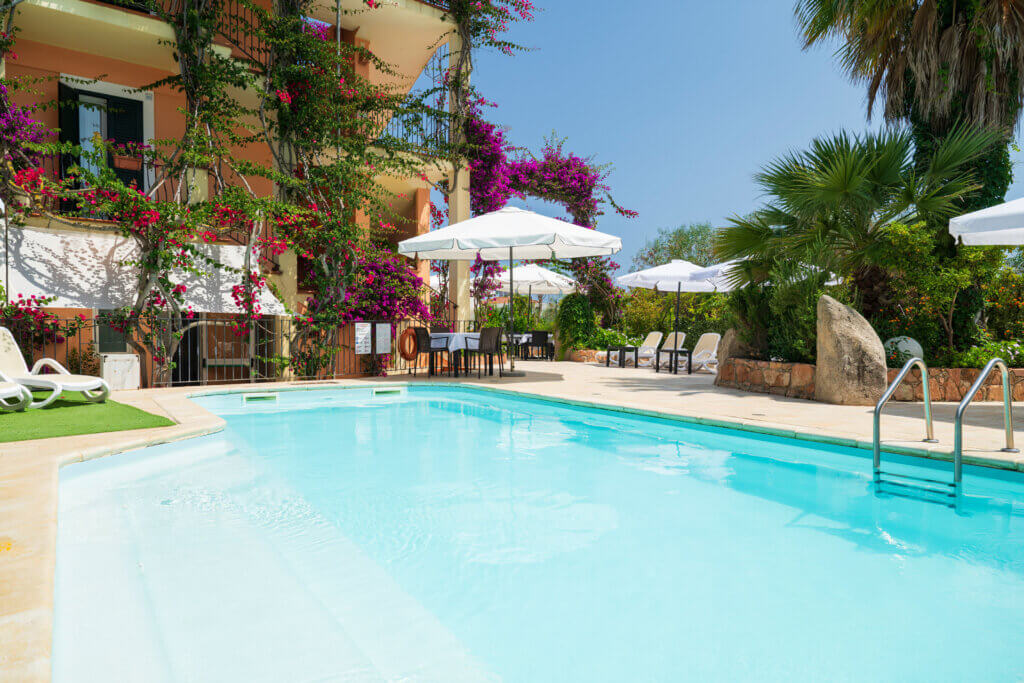 Galleria - Vista della piscina dell'Hotel Domus de Janas con lettini tavolini ed ombrelloni