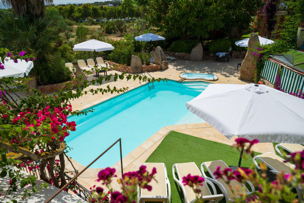Galleria - Piscina dell'Hotel Domus de Janas con lettini ed ombrelloni e grandi rocce per decorazione