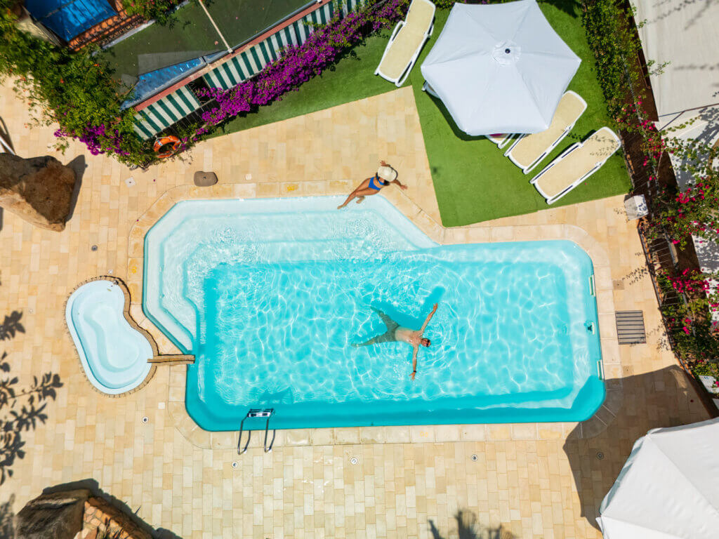 Galleria - La piscina dell'Hotel Domus de Janas con un ragazzo che si rilassa nell'acqua ed una ragazza seduta sul bordo piscina