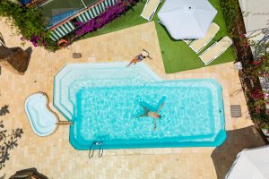 Galleria - La piscina dell'Hotel Domus de Janas con un ragazzo che si rilassa nell'acqua ed una ragazza seduta sul bordo piscina